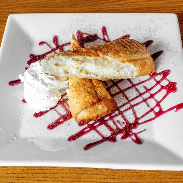 Two golden-brown churros, one cut open to reveal a creamy filling, with whipped cream and berry sauce.