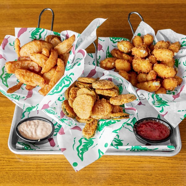 A tray of fried appetizers, including potato wedges, cheese curds, and fried pickles with dipping sauces.