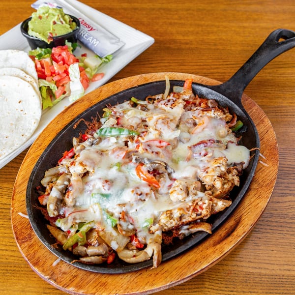 Sizzling chicken fajitas with melted cheese, bell peppers, and onions, served with guacamole, salad, and tortillas.