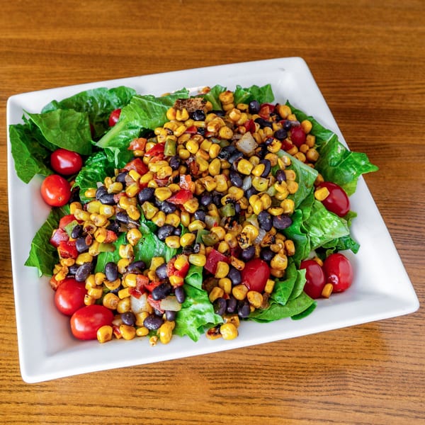 A vibrant Mexican salad with corn, black beans, bell peppers, and cherry tomatoes on a bed of lettuce.