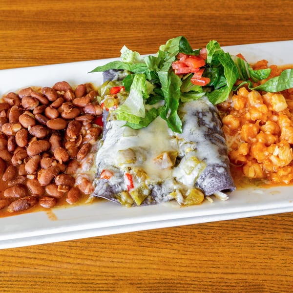 Mexican enchiladas with melted cheese, lettuce, tomatoes, pinto beans, and rice on a white plate.