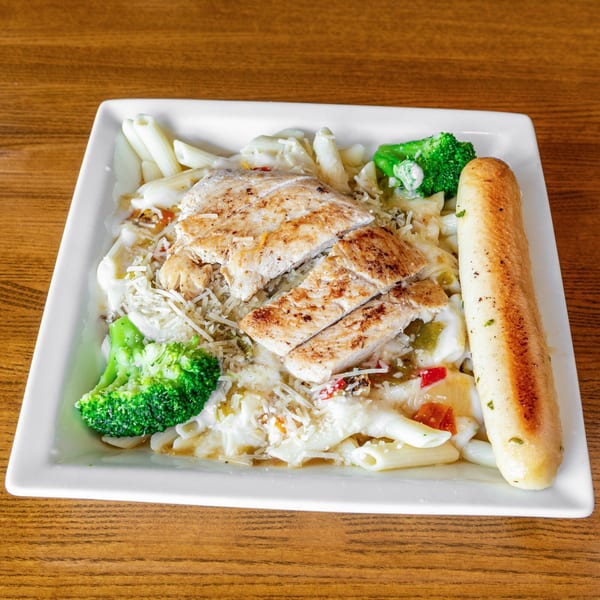 Grilled chicken and penne pasta with creamy sauce, broccoli, and a breadstick on a white plate.