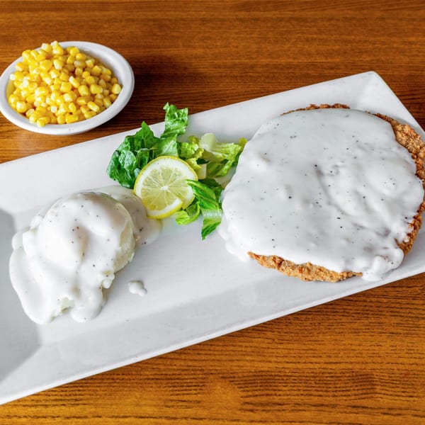 Chicken fried steak with gravy, mashed potatoes, corn, and a side salad with lemon.